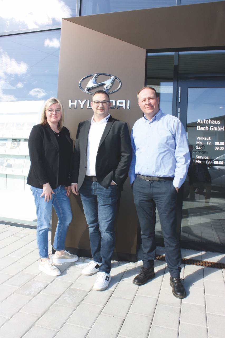 Drei Personen vor dem Eingang des neu erbauten Hyundai Autohauses bei der Übergabe