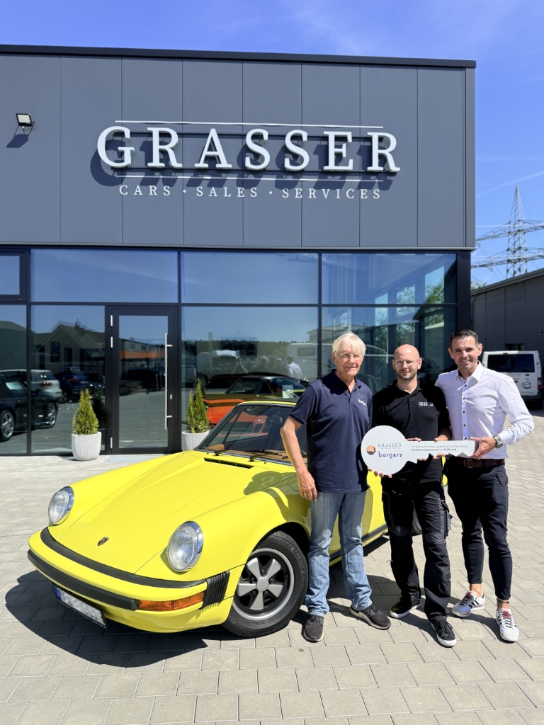 drei Personen mit Schlüssel in der Hand vor gelbem Porsche