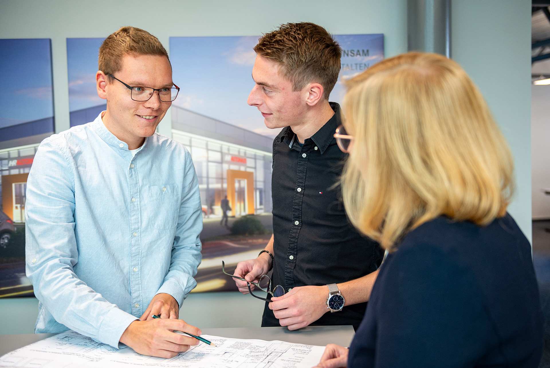 Drei Personen, zwei Männer und eine Frau, besprechen Baupläne an einem Tisch
