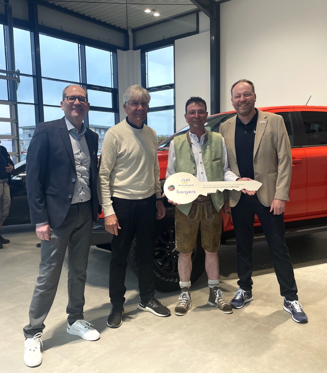 vier Männer mit einem Schlüssel in der Hand, rotes Auto im Hintergrund